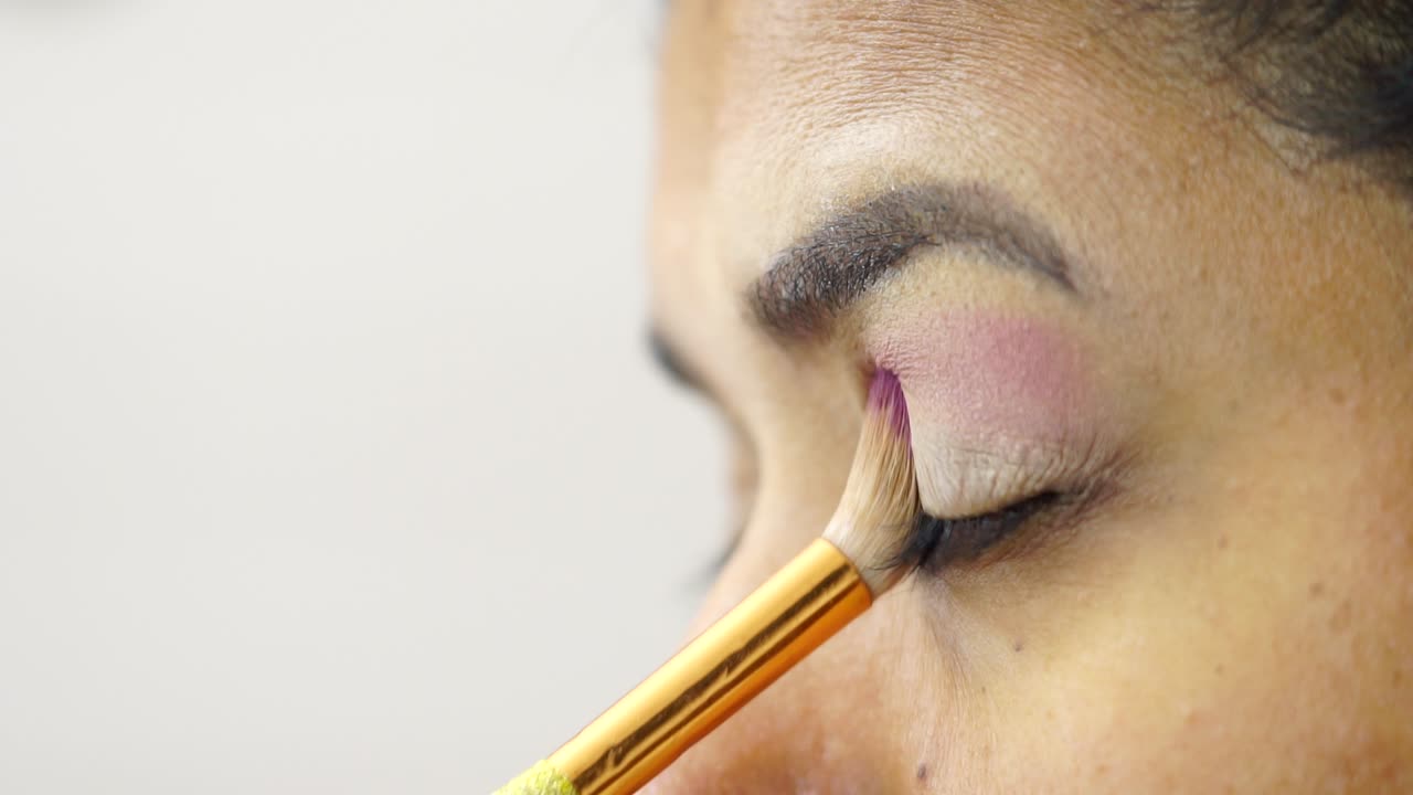 Side close-up of brown-eyed girl applying pink eye shadow with brush