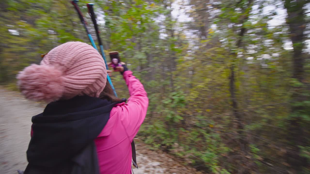 chica de senderismo con palos y mochila en un camino o sendero en el bosque de montaña. tomando fotos de sí misma con su teléfono celular. viajes y estilo de vida saludable al aire libre en la temporada de otoño. movimiento circular de la cámara..