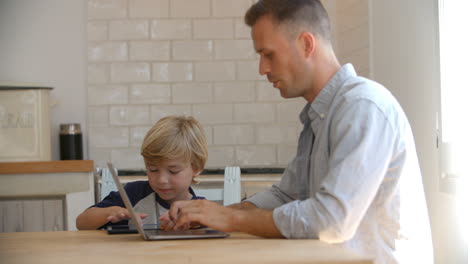 father and son using computers at the kitchen table