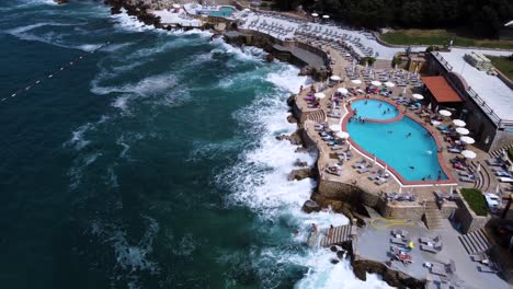 bar club with pool on concrete shore with waves crashing, aerial