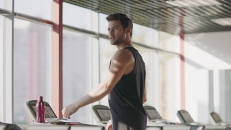 handsome man looking around in fitness club. macho male walking treadmill in gym