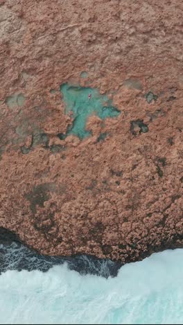 una toma vertical de las olas del mar chocando contra el acantilado