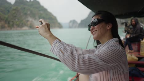 woman taking a photo on a boat trip amidst a scenic mountain landscape