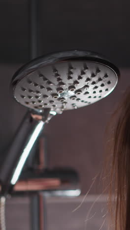 woman waits while water starts to run in shower cabin closeup. lady stands near shower head with falling liquid drops in home bathroom. body care