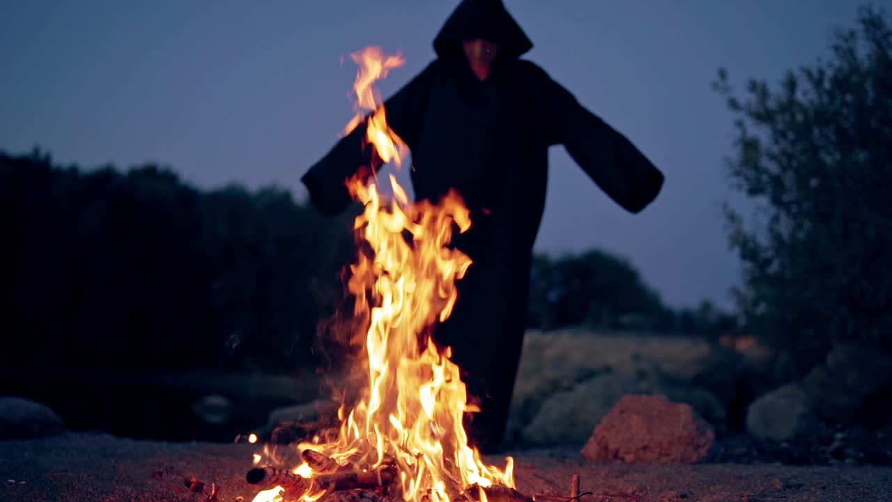 Fire flame on the dark background with black figure. Silhouette of death near the fire in the evening. Scary atmosphere at Halloween.
