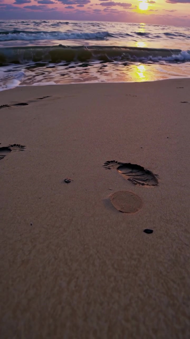 Onde marine che cancellano le impronte su una spiaggia sabbiosa al tramonto