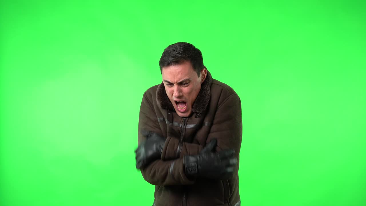 Man shivering and rubbing hands to keep warm on a green screen