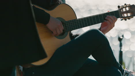 closeup still clip of person playing strings on guitar outdoors, with river delta reflections on background. high contrast makes person main subject.