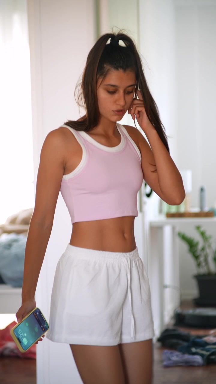 Giovane donna che si sistema i capelli e il top mentre usa lo smartphone