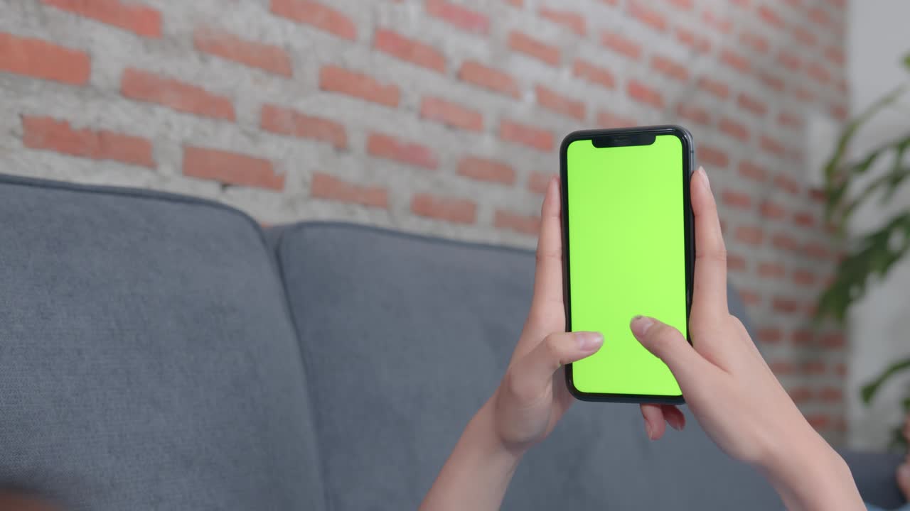 mujer sosteniendo una maqueta de pantalla verde de teléfono inteligente con un mensaje de tipo en el sofá en casa.