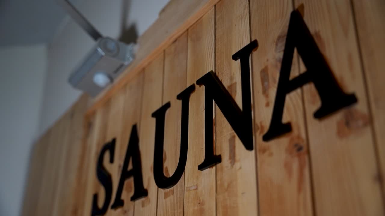 Letras negras de "sauna" montadas en paneles verticales de pared de madera en el interior de un spa.