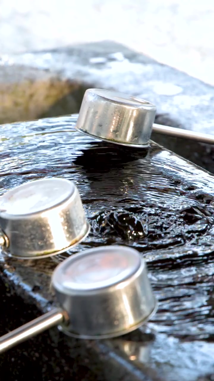 Primo piano di mestoli di metallo che riposano su una vasca di pietra con acqua che scorre in Giappone.