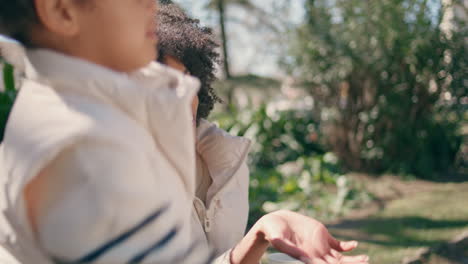 smiling child throwing seeds to birds in park close up. mother looking