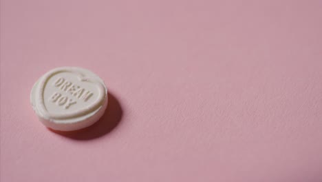 mano recogiendo caramelos de corazón con mensaje romántico dream boy sobre fondo rosa