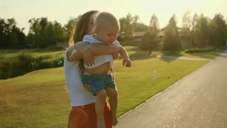 Mother-holding-little-son-on-hands-in-park.Toddler-looking-soap-bubbles-outdoors