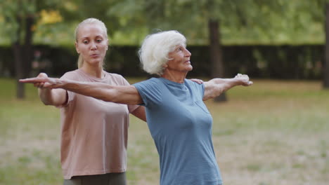 female fitness coach helping senior woman during outdoor workout