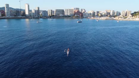 Toma-Aérea-De-Un-Bote-De-Remos-Y-Yates-En-El-Mar-Con-Un-Fondo-De-Ciudad