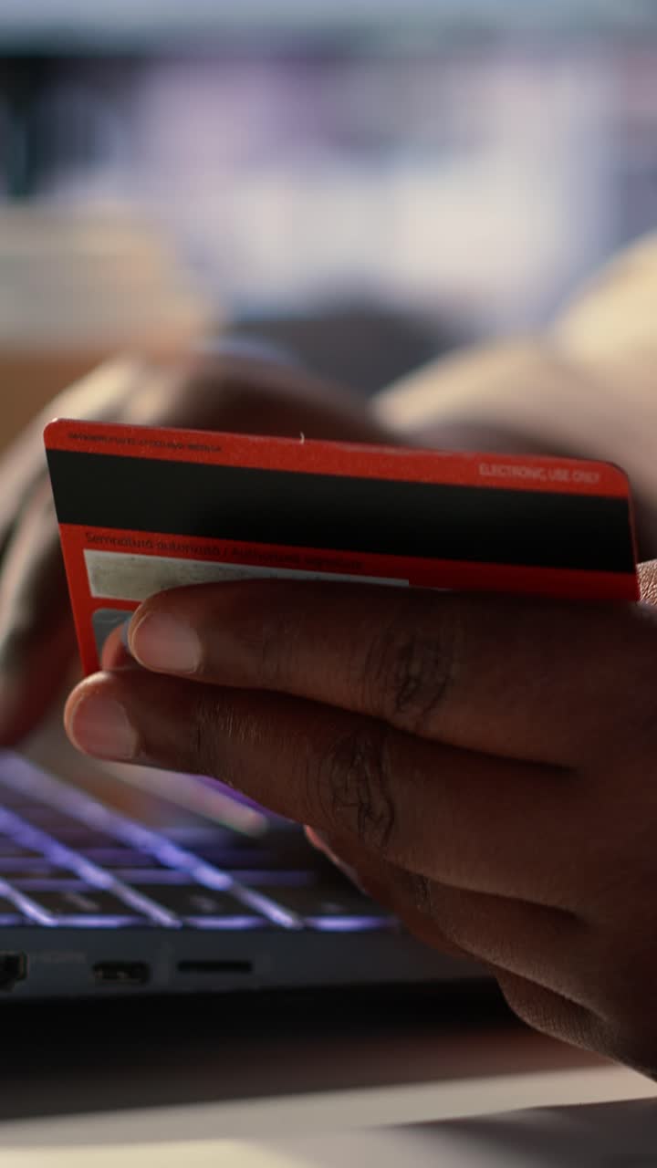 Primo piano di una mano che tiene una carta di credito mentre digita al laptop per acquisti online