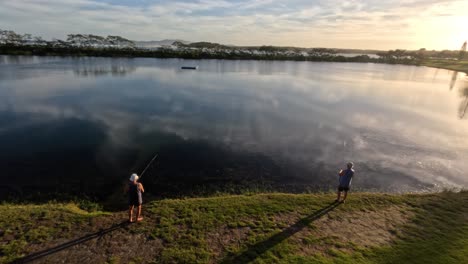 person fishing by a calm lake during sunset