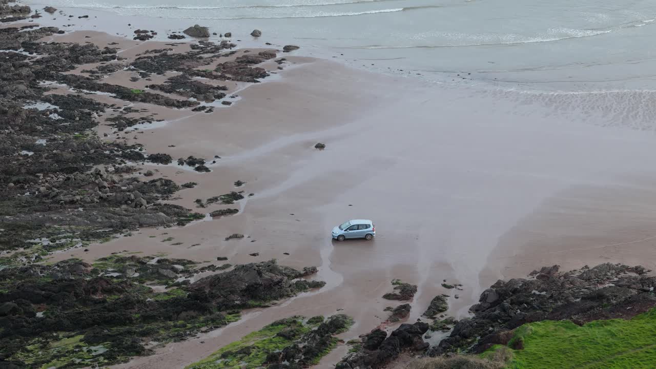 Car parked on sleeping bay sandy beach cove in Milford Haven aerial view looking down from cliff