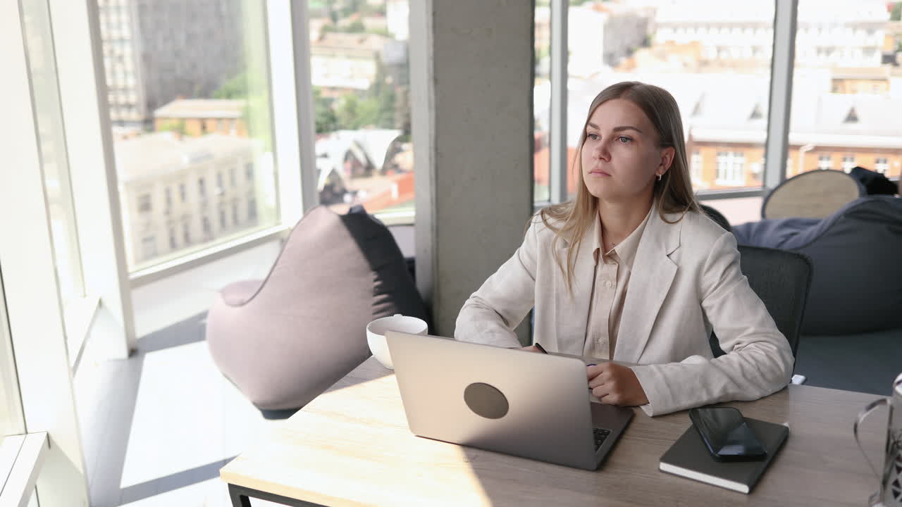 Bella giovane donna con gli occhiali seduta a un tavolo in ufficio e che lavora al laptop. Una donna d'affari parla al telefono al lavoro.