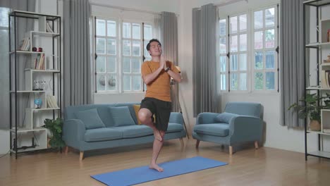 el hombre asiático no puede hacer yoga en la postura del árbol en la alfombra en casa