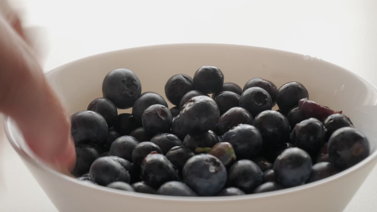 Fresh blueberries being picked from a bowl, close-up shot showing hand selecting berries