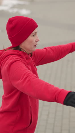 mujer con capucha roja y guantes realizando la mano se extiende al aire libre en el camino cubierto de nieve con valla metálica decorativa en el entorno de invierno en la atmósfera de clima frío