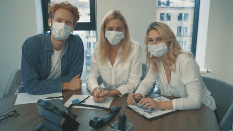 junge geschäftsfrauen und mann mit gesichtsmaske, die im büro in die kamera blicken