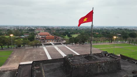 large vietnamese flag atop the flag tower of hue citadel, facing the ngo mon gate and imperial city beyond, central vietnam, captured by dolly-in drone shot