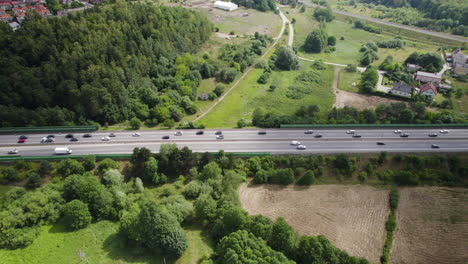 Vista-De-Seguimiento-Aéreo-Del-Tráfico-De-Vehículos-Pesados-En-La-Carretera-Rural-De-Varios-Carriles,-Rodeada-De-árboles-De-Tierras-Verdes-Y-Casas-Suburbanas-En-Gdynia,-Polonia