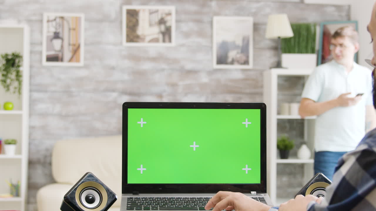 Man working on laptop with green screen at home