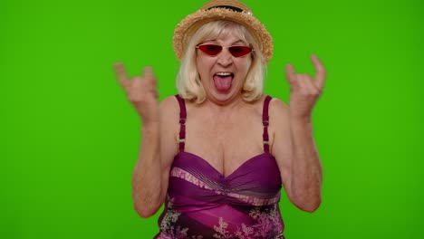 Senior-woman-tourist-in-swimsuit-dancing,-celebrating,-showing-tongue,-rock-and-roll-hand-gesture