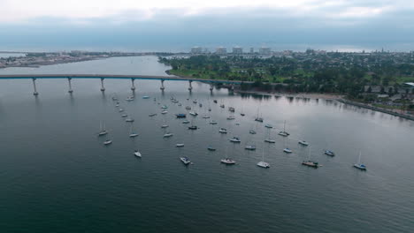 Flying-towards-small-white-boats-parked-near-Coronado-island-and-Coronado-bridge-in-San-Diego-Bay