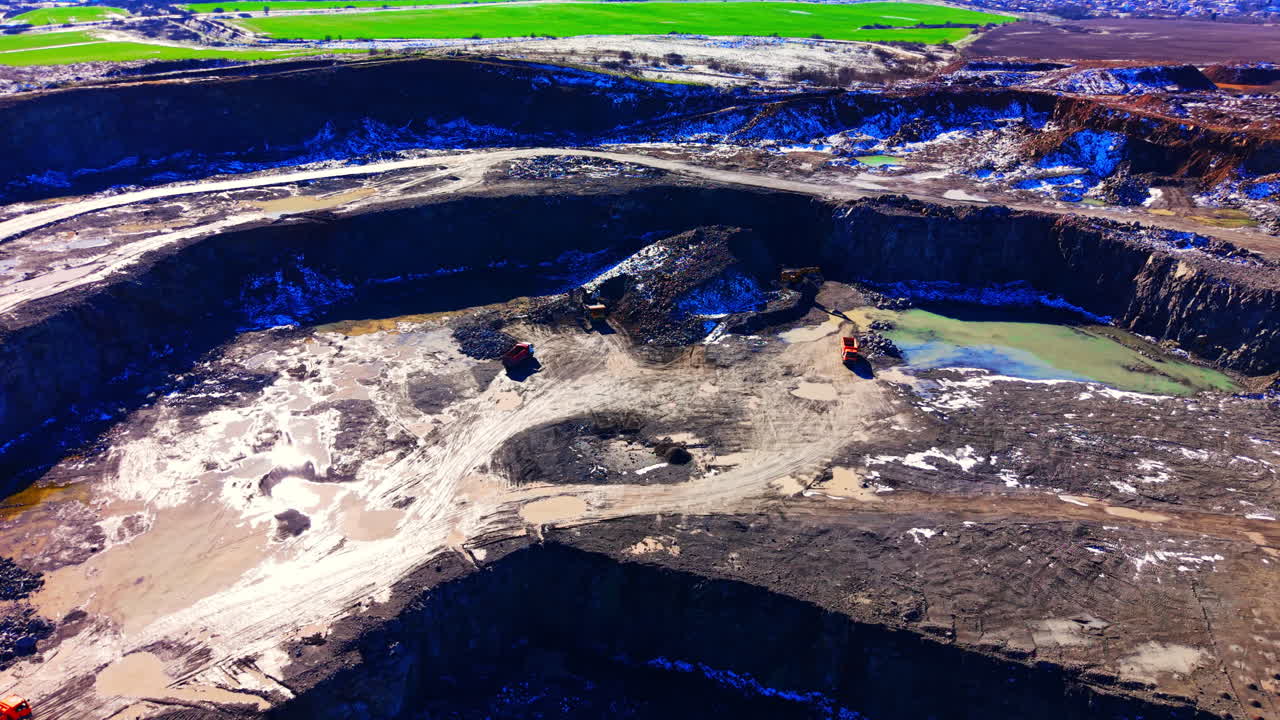 Stone quarry with excavators, trucks, and terraced landscape under bright daylight. Aerial view of open pit mine with heavy machinery