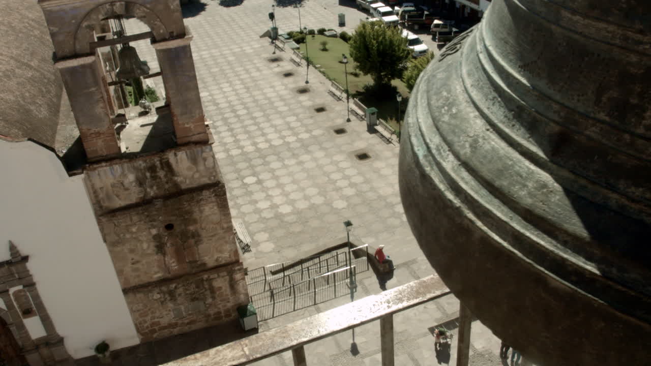 campanas de iglesia montadas en una torre alta en la plaza pública de un pequeño pueblo mexicano, que pueden ser escuchadas por la comunidad circundante