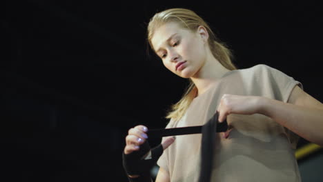 Serious-female-athlete-preparing-for-boxing-at-gym.-Fit-girl-wrapping-hands