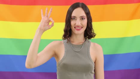 woman making an ok gesture in front of a rainbow pride flag
