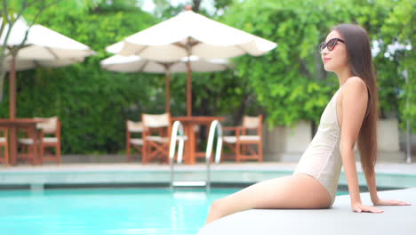 while sitting on the edge of a swimming pool which her feet in the water enjoying the ambiance of the resort