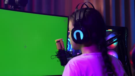 close up back view of asian girl streamer feeling disappointed fails game over on green screen computer. live stream on desk illuminated by rgb led strip light