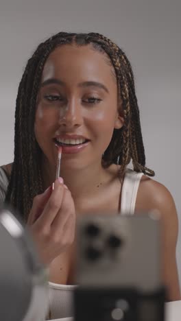 joven grabando belleza maquillaje revisión o tutorial para brillo de labios en teléfono móvil para cargar en el canal de redes sociales
