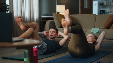 Couple training abs lying with spinning legs like bicycle in apartment together.