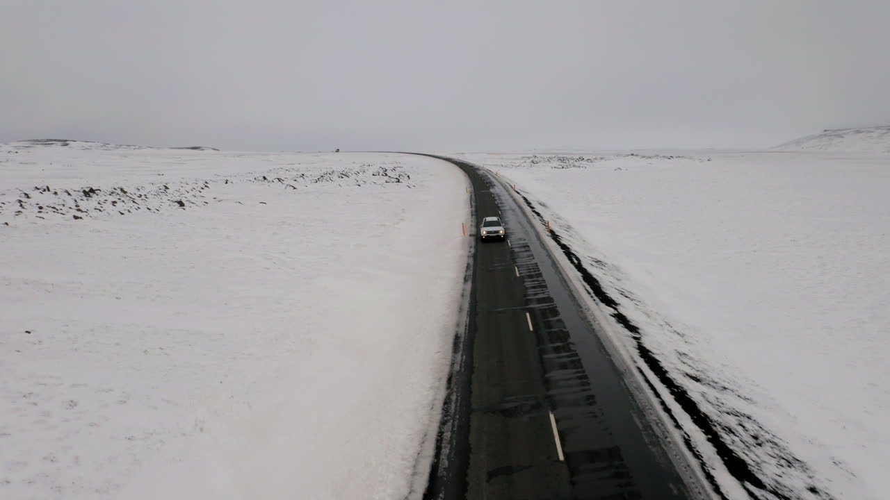 공중 프론트 뷰: 한 차가 눈  ⁇ 인 도로를 달리고 있다
