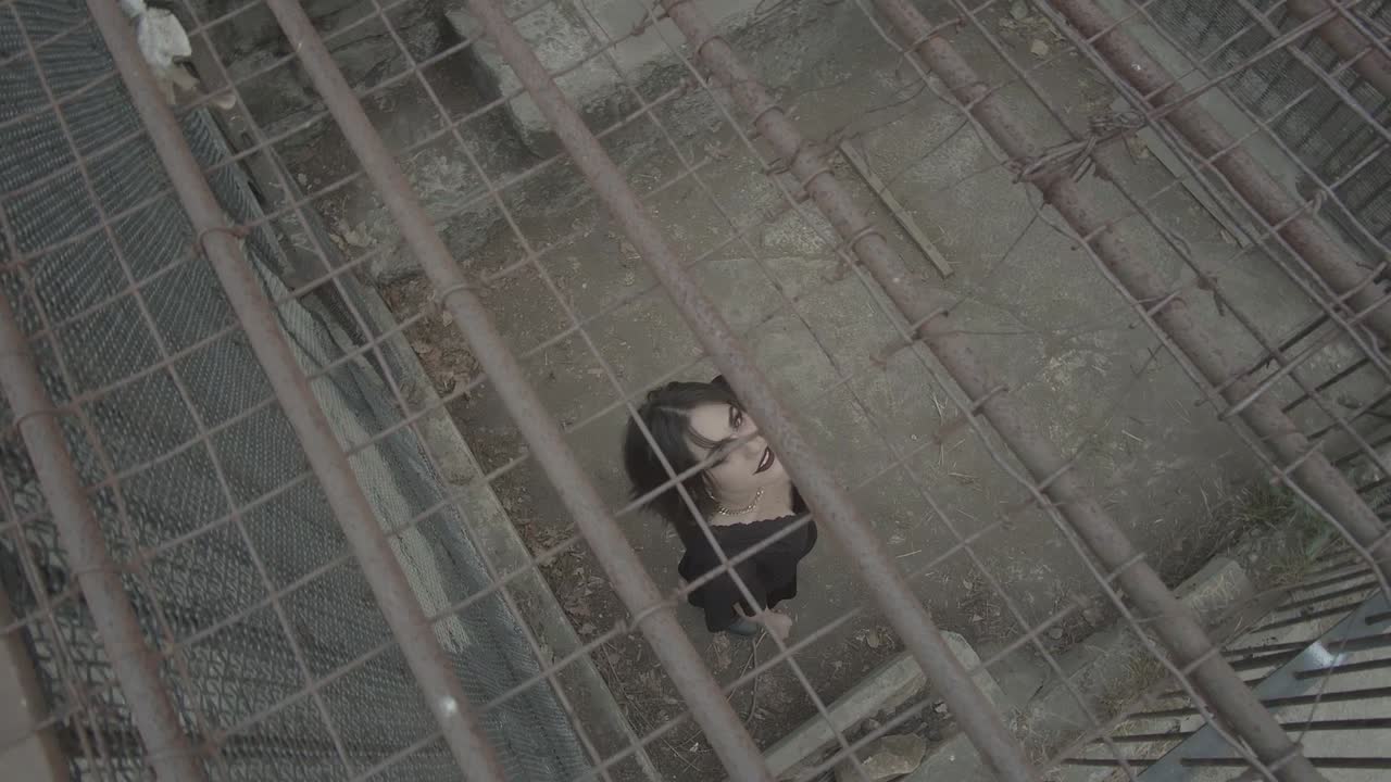 창백한 피부와 검은 화장을 하고 옷을 돌고 감옥에서 올려다보는 무서운 여성