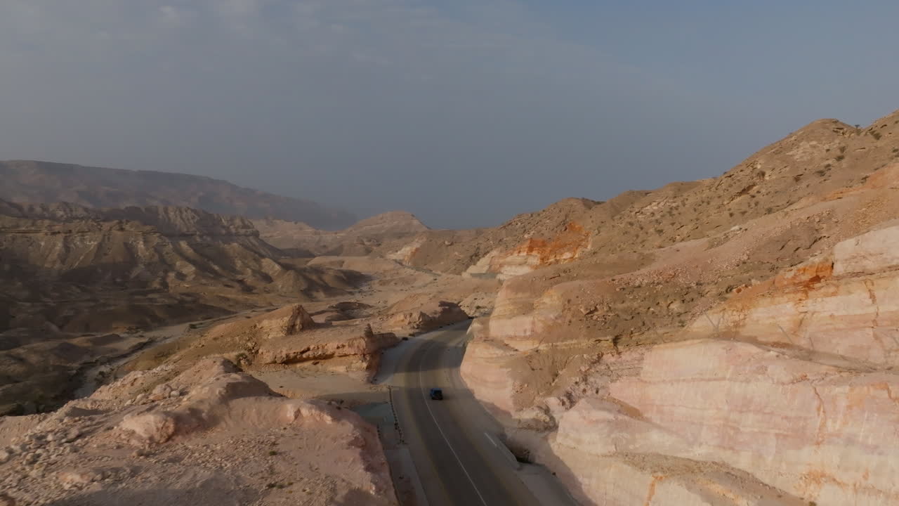 Winding coastal road through rocky hills with a vehicle driving in Oman’s desert