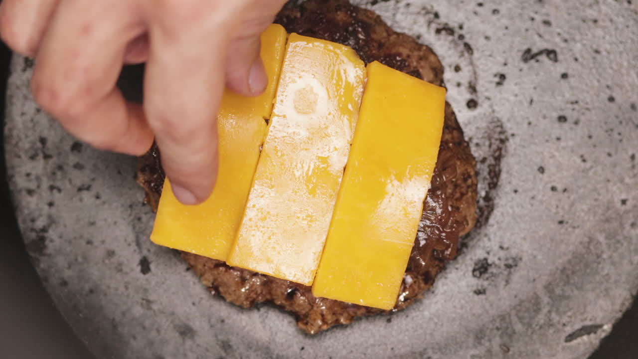 Vue rapprochée du dessus sur la main d'un homme ajoutant trois tranches de fromage cheddar sur un steak haché grillé chaud