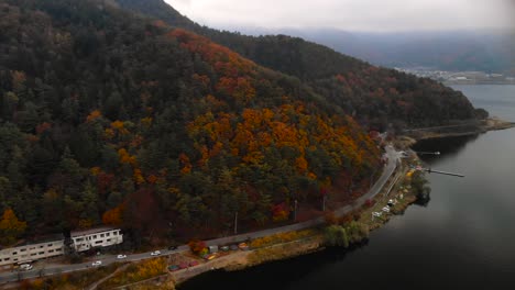 Aerial-over-cars-driving-on-road-next-to-autumn-colored-trees-and-lake