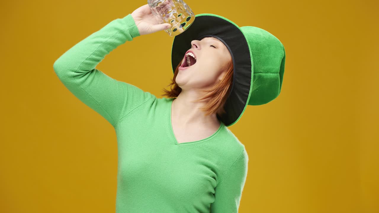 Young woman with leprechaun's hat drinking beer in studio shot