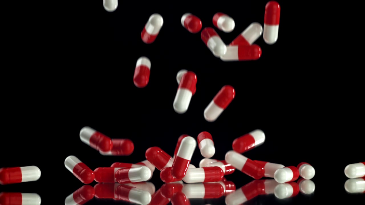 Capsule medicinali rosse e bianche che cadono su una superficie nera riflettente