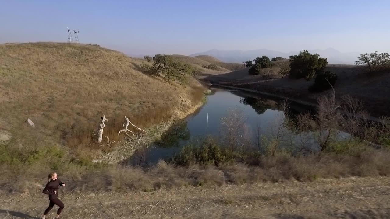 женщина бежит вдоль красивого озера во время вечерней съемки с помощью беспилотного летательного аппарата